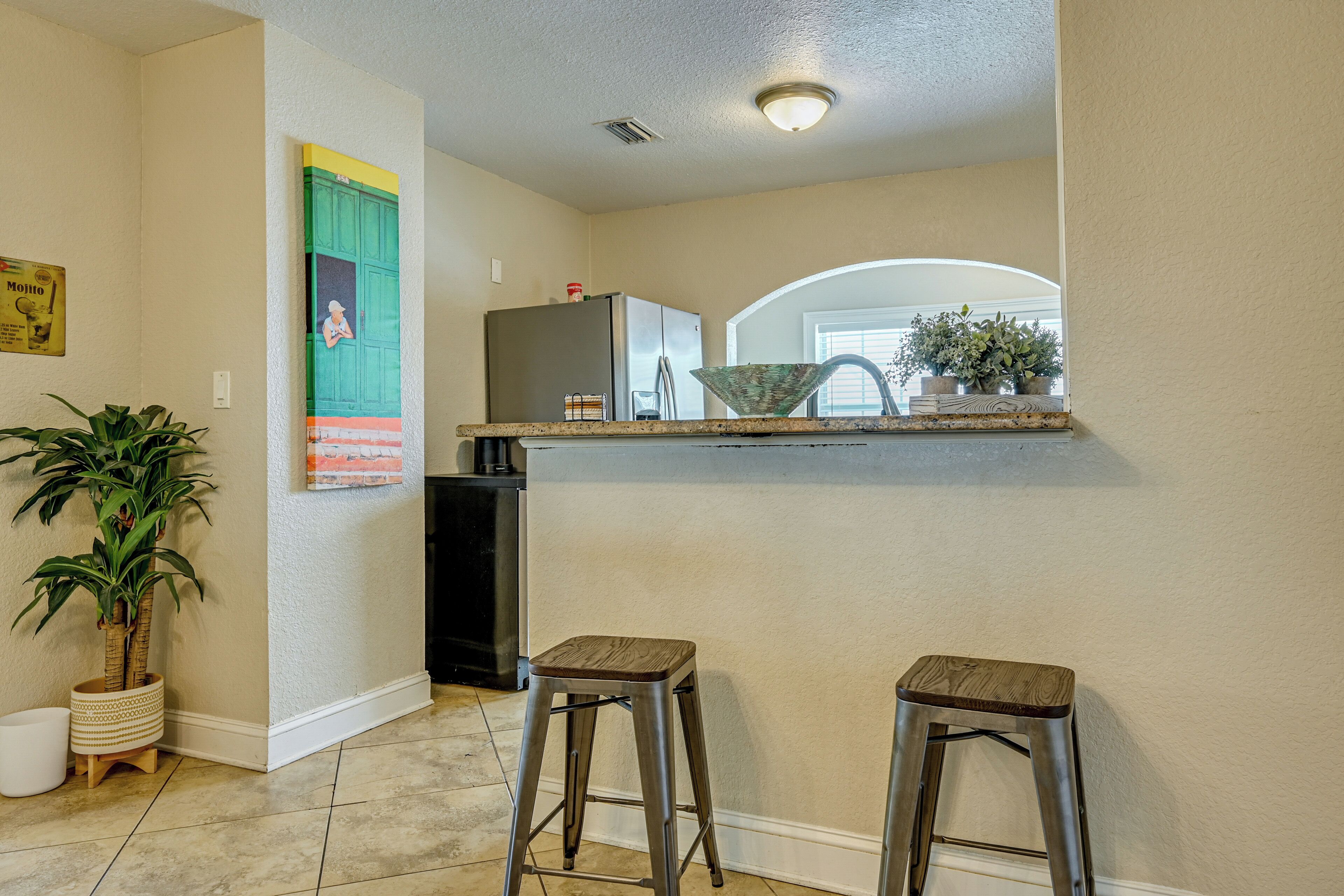 A kitchen with a refrigerator, two stools, and a potted plant.