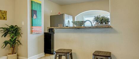 A kitchen with a refrigerator, two stools, and a potted plant.