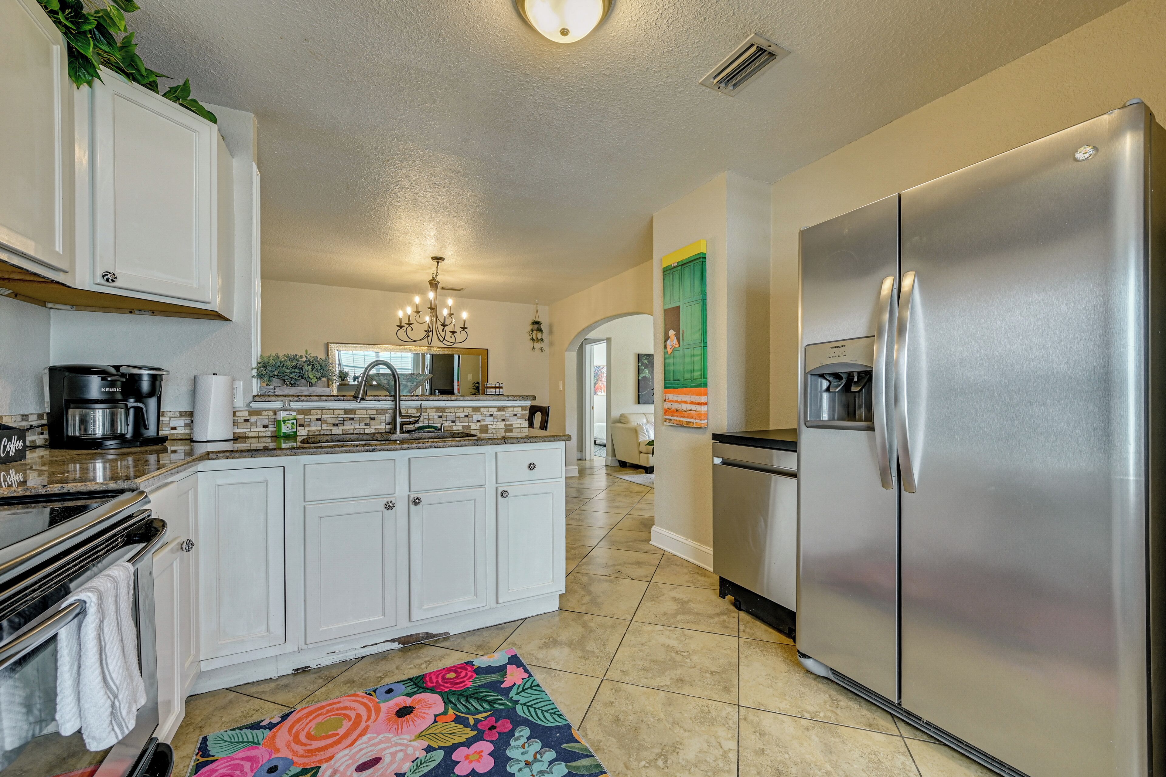 A kitchen with white cabinets, a stainless steel refrigerator, a coffee maker, and a patterned rug.