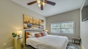A bedroom with a bed, a ceiling fan, a window with blinds, a wall-mounted TV, and a painting. - Backyard Fun & Dtwn Exploring: Family Gem in Tampa (Tampa)