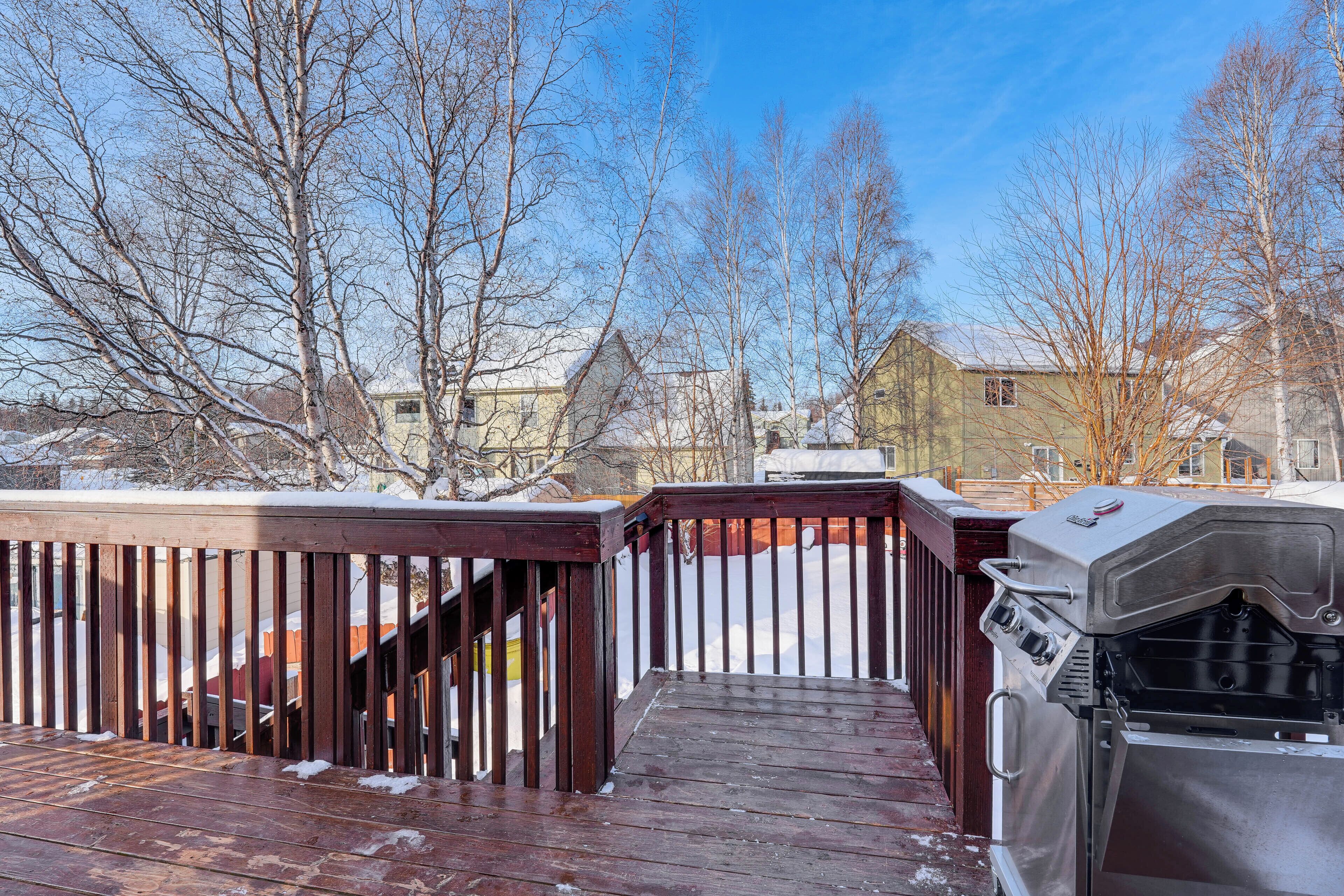 A wooden deck with a grill and snow-covered ground.