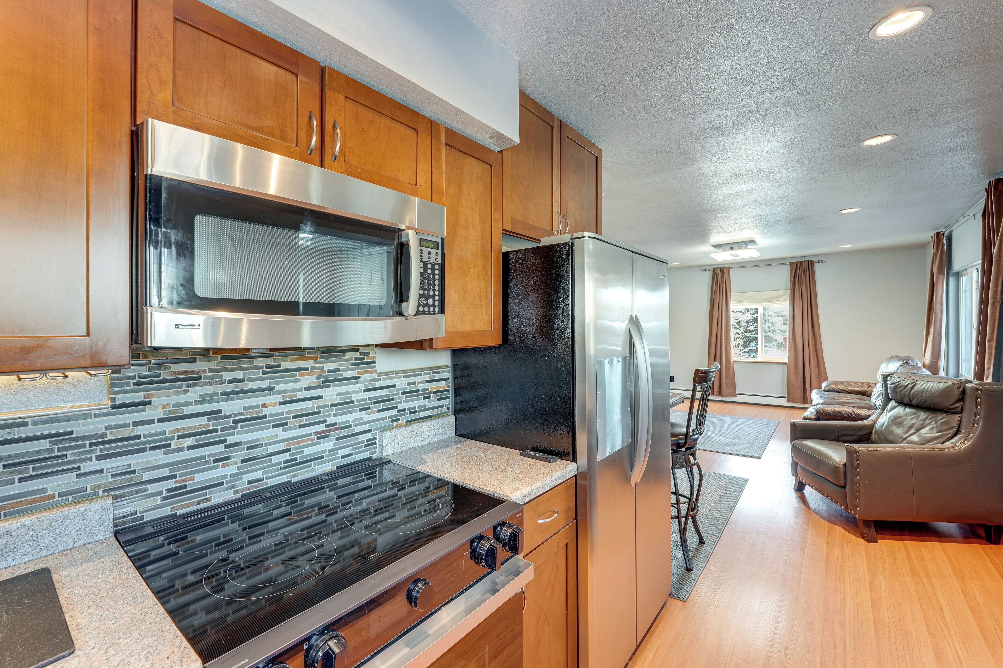A modern kitchen with stainless steel appliances, wooden cabinets, and a stone backsplash.