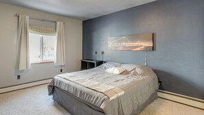 A bedroom with a bed, a nightstand, a lamp, a window with curtains, and a painting of a bridge on the wall. - Hike, Bike & Ski! Cozy Anchorage Townhome (Anchorage)
