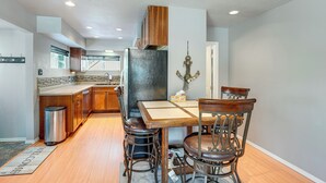 A modern kitchen with wooden cabinets, a stainless steel refrigerator, and a dining area with a wooden table and metal chairs. - Hike, Bike & Ski! Cozy Anchorage Townhome (Anchorage)