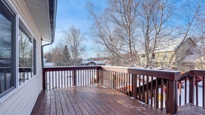A wooden deck with a railing, a snow-covered ground, and leafless trees in the background. - Hike, Bike & Ski! Cozy Anchorage Townhome (Anchorage)