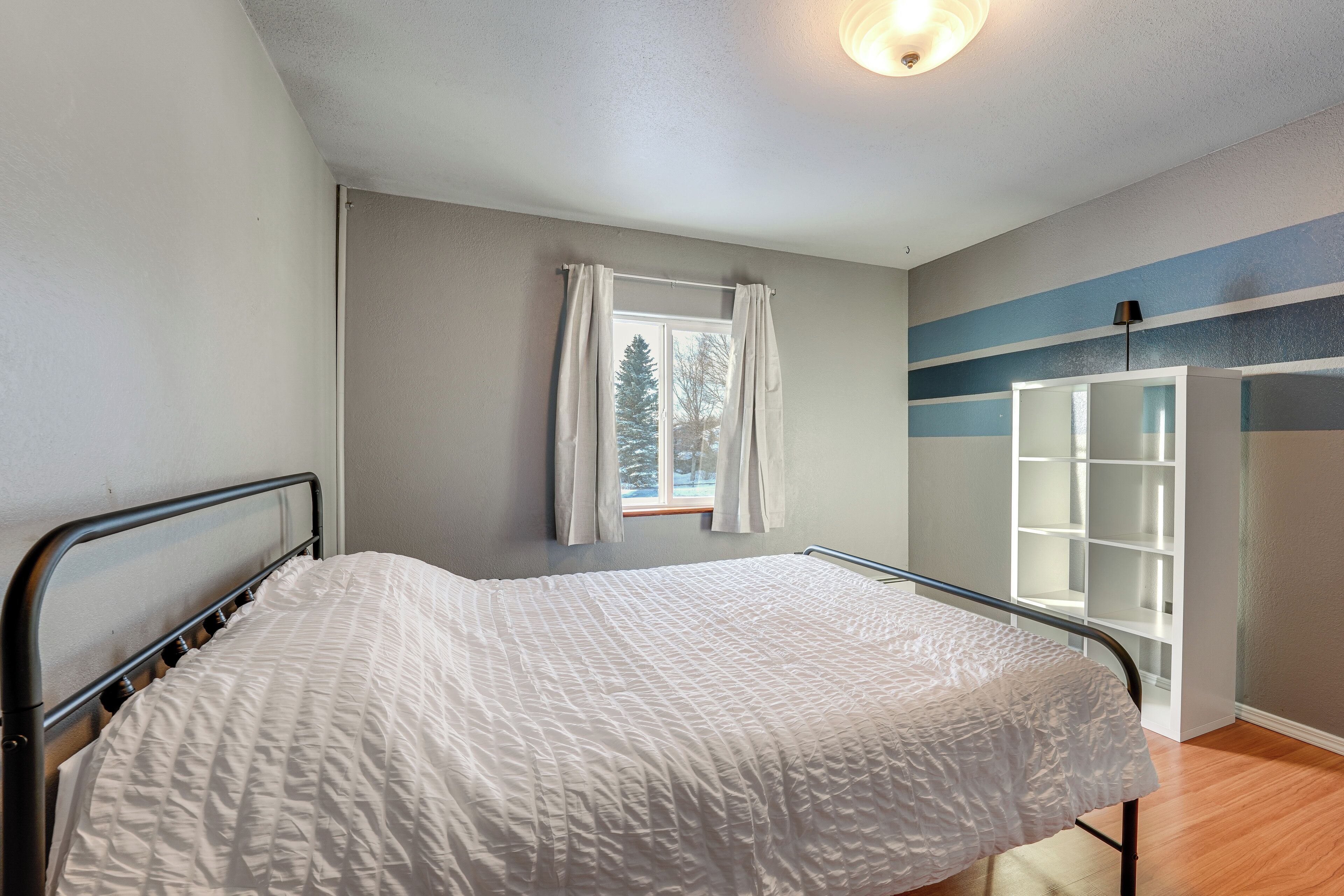 A bedroom with a bed, a window with curtains, a white wardrobe, and a blue-striped wall.