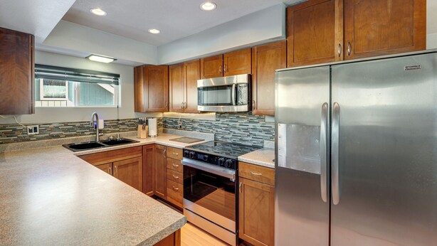 A modern kitchen with wooden cabinets, stainless steel appliances, and a granite countertop. - Hike, Bike & Ski! Cozy Anchorage Townhome (Anchorage)