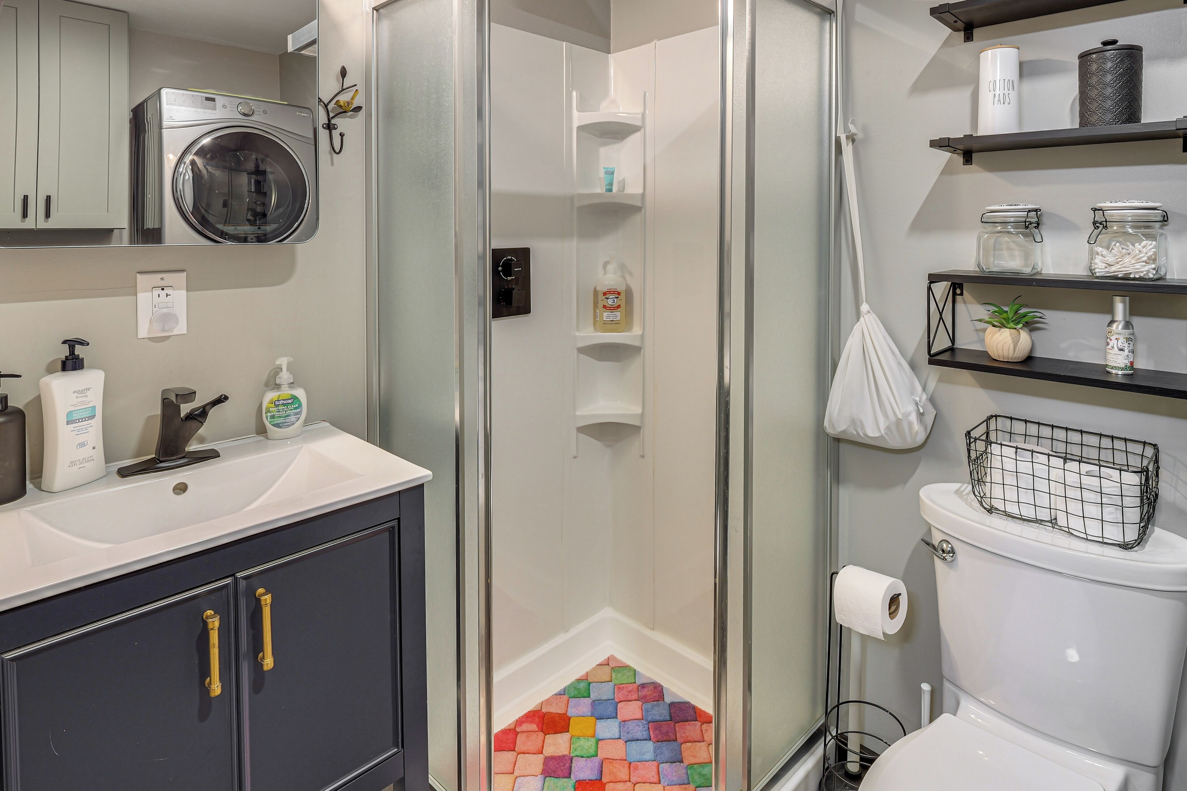 A bathroom with a shower, toilet, and sink. There are shelves with toiletries and a hanging towel rack.