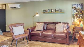 A living room with a brown leather sofa, a brown leather armchair, a floor lamp, a framed picture collection on the wall, and a painting of sunflowers.