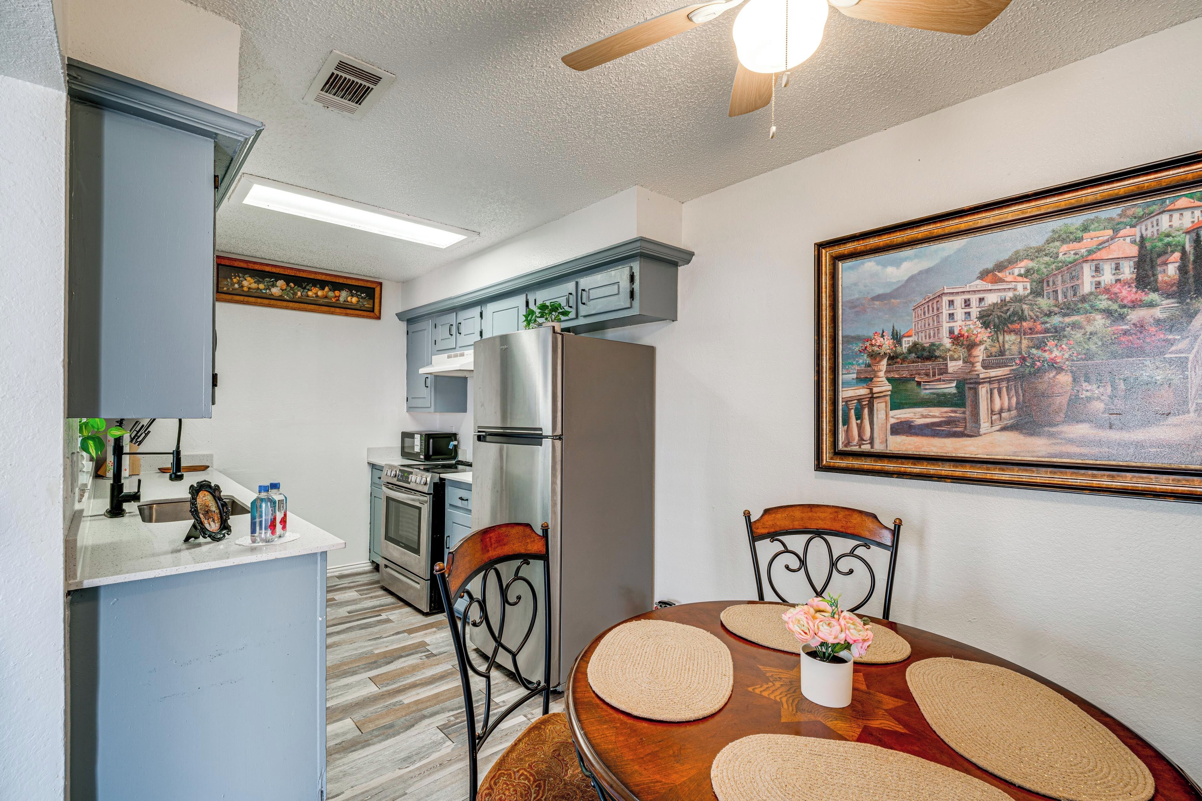 A compact kitchen with modern appliances, a dining area with a wooden table and chairs, and a painting on the wall.