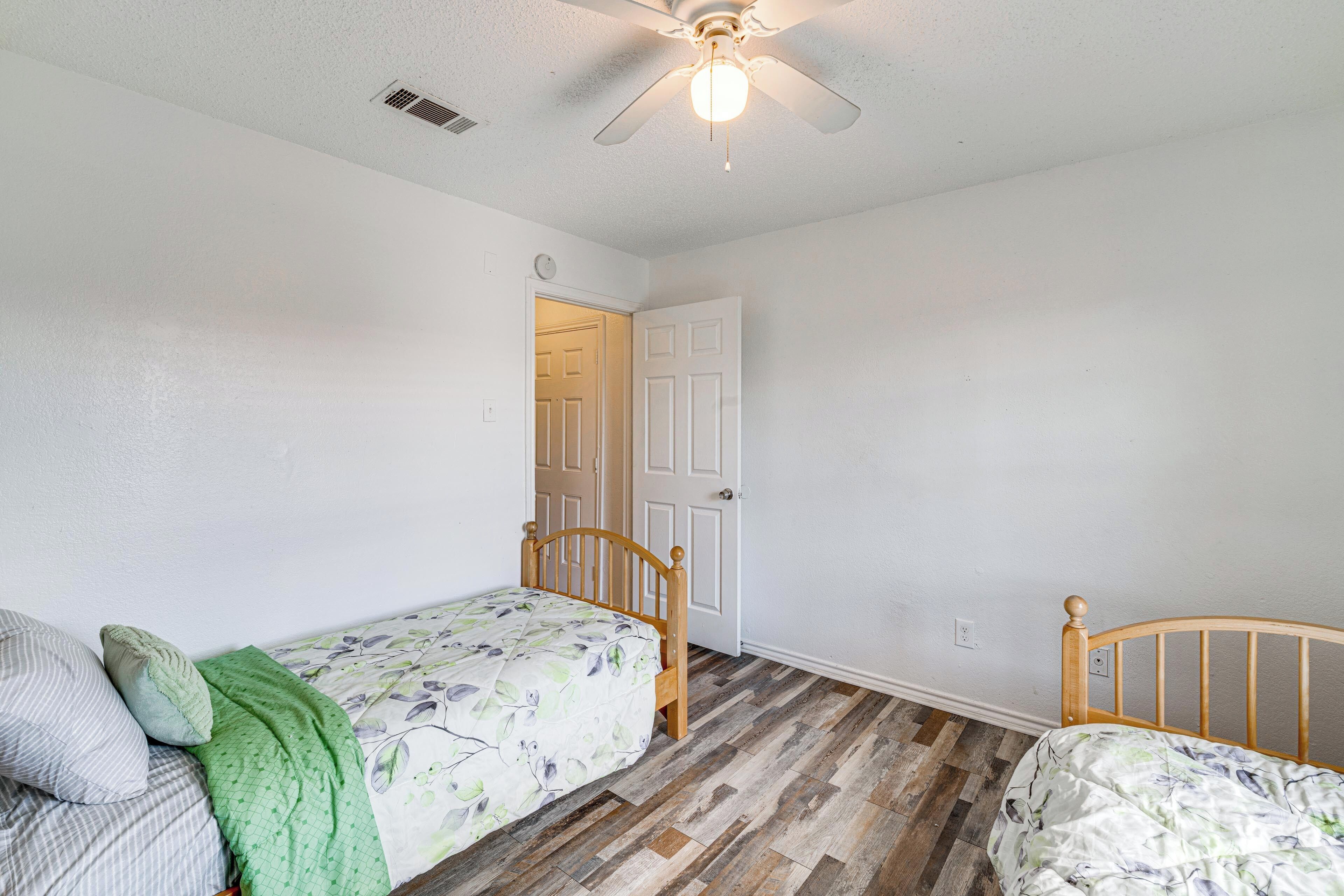 Un dormitorio con dos camas de madera, un ventilador de techo y una puerta a otra habitación.