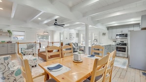 Cocina amplia con armarios blancos, un microondas y un horno. Hay un comedor con mesa y sillas de madera, y una ventana con vistas a la cocina.