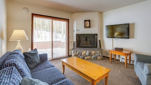 A living room with a stone fireplace, a television mounted on the wall, a sofa, and a coffee table. - 3 Mi to Winter Park Slopes! Unit w/ Pool & Hot Tub (Winter Park)