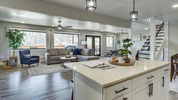 A spacious living area with a large island, a staircase, and a view of the outdoors.