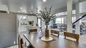 A modern kitchen with white cabinets, a dining table with chairs, a vase with dried plants, and a staircase leading to another level.