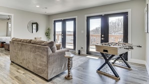 A living room with a sofa, a foosball table, and a large window.
