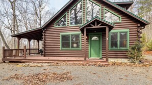 Une cabane en rondins avec un porche, une porte verte et de grandes fenêtres.