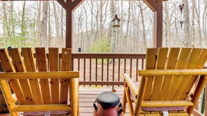 Une terrasse en bois avec deux fauteuils Adirondack donnant sur une zone boisée.