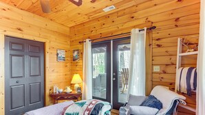 Une pièce chaleureuse, aménagée dans une cabane en bois, avec un lit, une chaise, une table avec une lampe et une porte-fenêtre coulissante donnant sur un espace extérieur.