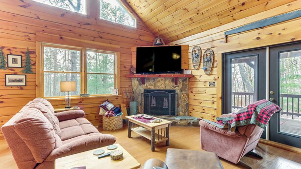Un intérieur de chalet chaleureux avec des murs en bois, une cheminée, un téléviseur et des sièges confortables.