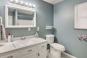 Un baño con tocador blanco, un espejo grande con luces, un inodoro y un perchero con toallas.