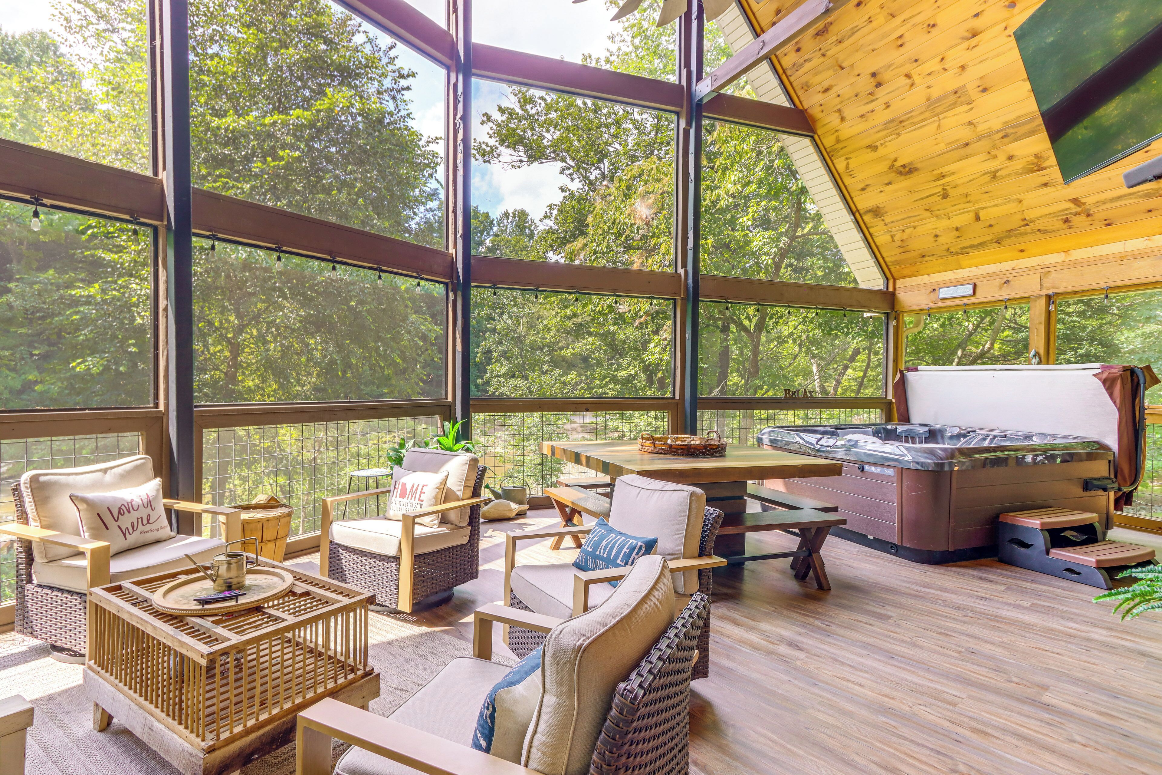 A spacious outdoor deck with wicker furniture, a hot tub, and a view of the surrounding trees.