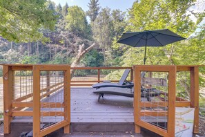 Eine Holzterrasse mit Metallgeländer, einem schwarzen Sonnenschirm und zwei Liegestühlen.