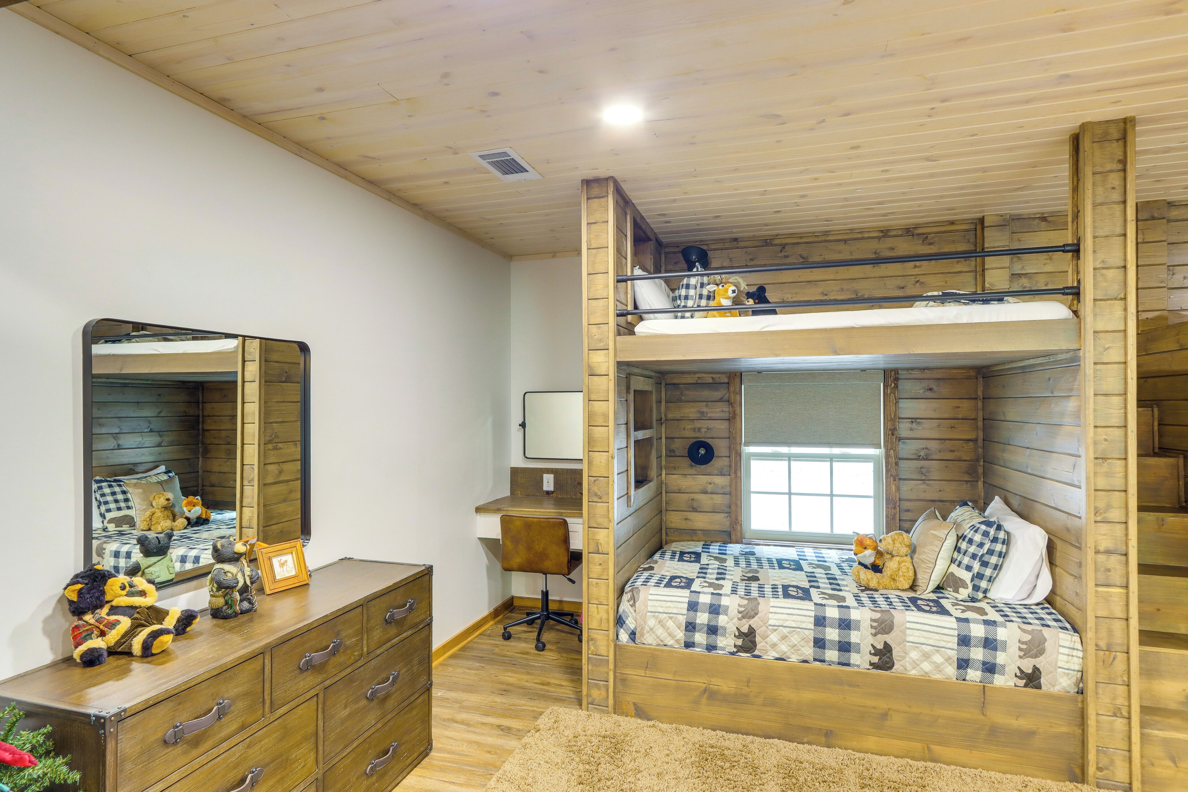A bunk bed with a checkered bedspread, a dresser with drawers, a mirror, and stuffed animals.