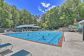 Ein Schwimmbad mit Liegestühlen und einem überdachten Bereich, umgeben von Bäumen.