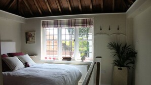 A bedroom with a large bed, a window with a view of the outside, a plant, and a radiator. - The Gazebo - Winchelsea Town (East Sussex)