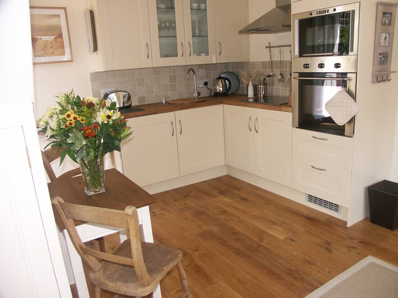 A kitchen with white cabinets, a wooden countertop, a sink, a stove, and a vase with flowers on the table.