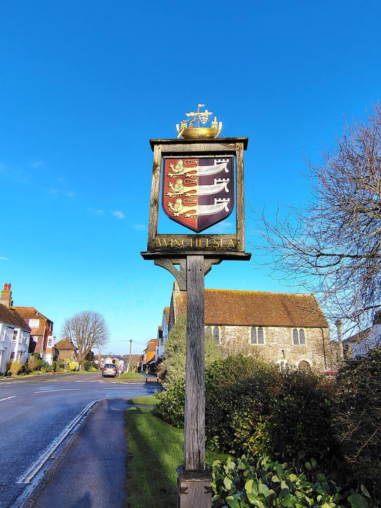 A sign with a coat of arms and the text "WINE HELLIS A" on a wooden post.