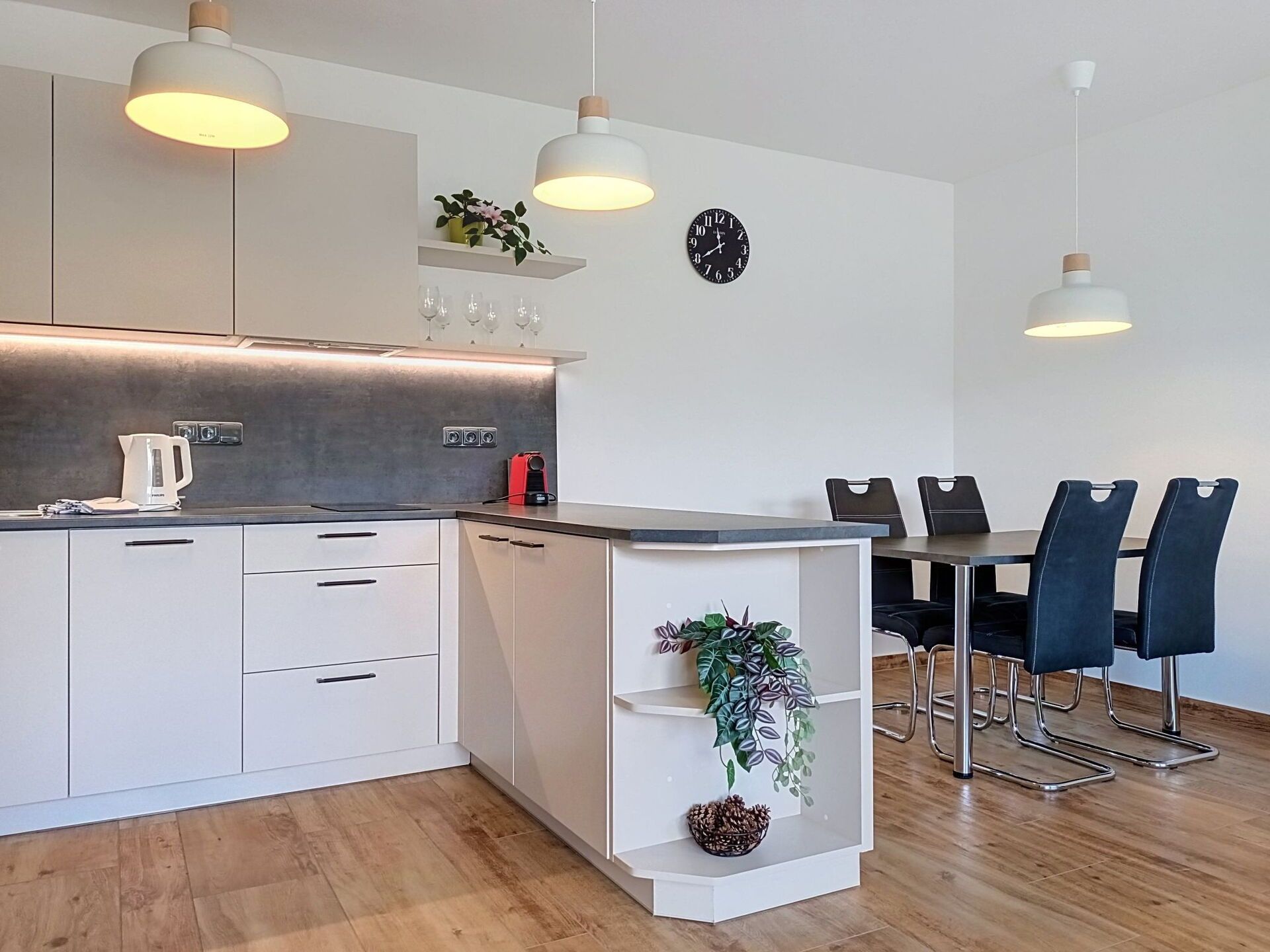 Une cuisine moderne avec des meubles blancs, une machine à café et une horloge au mur.