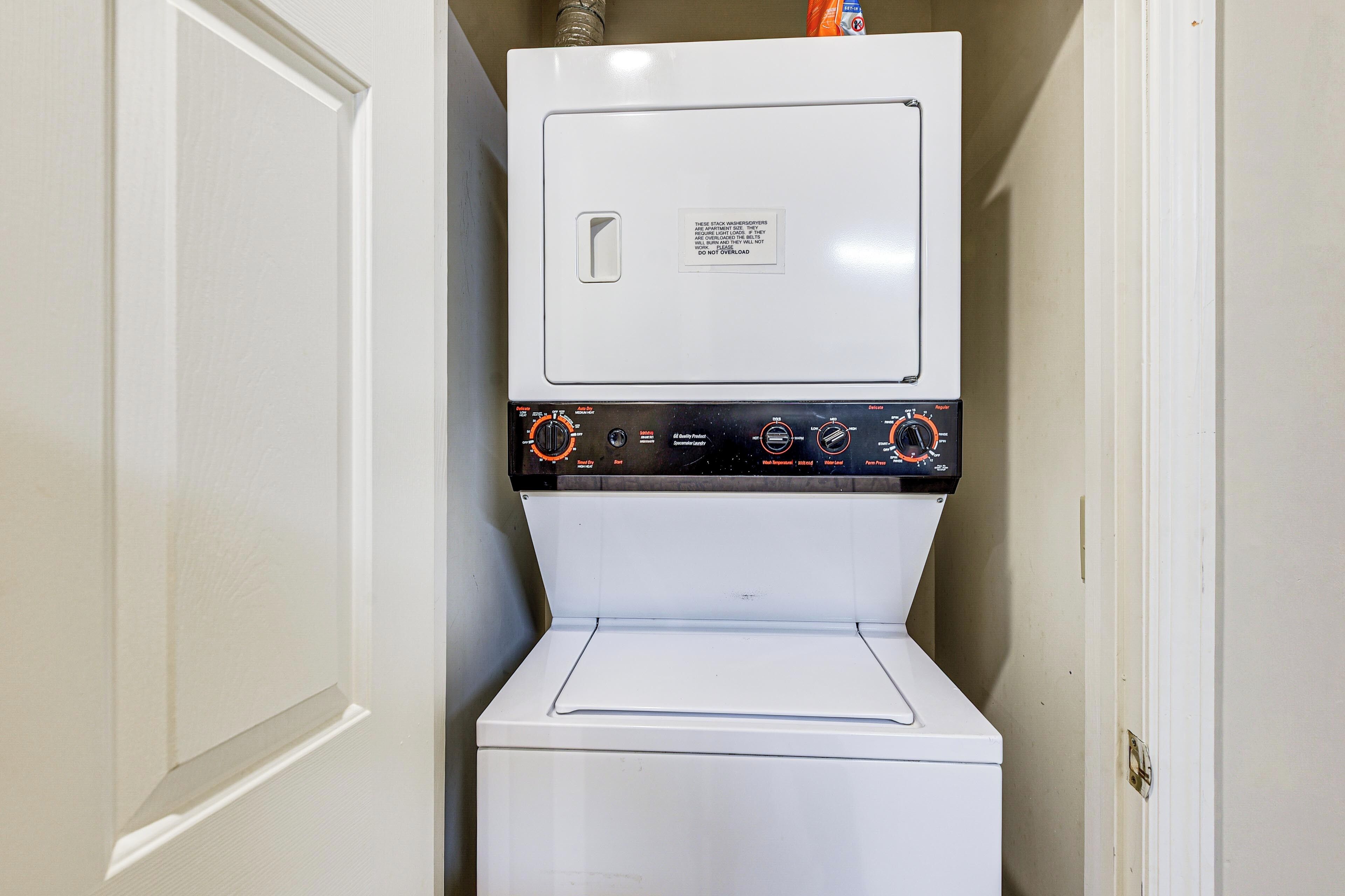 A compact washer and dryer unit in a small laundry room with a door on the left.