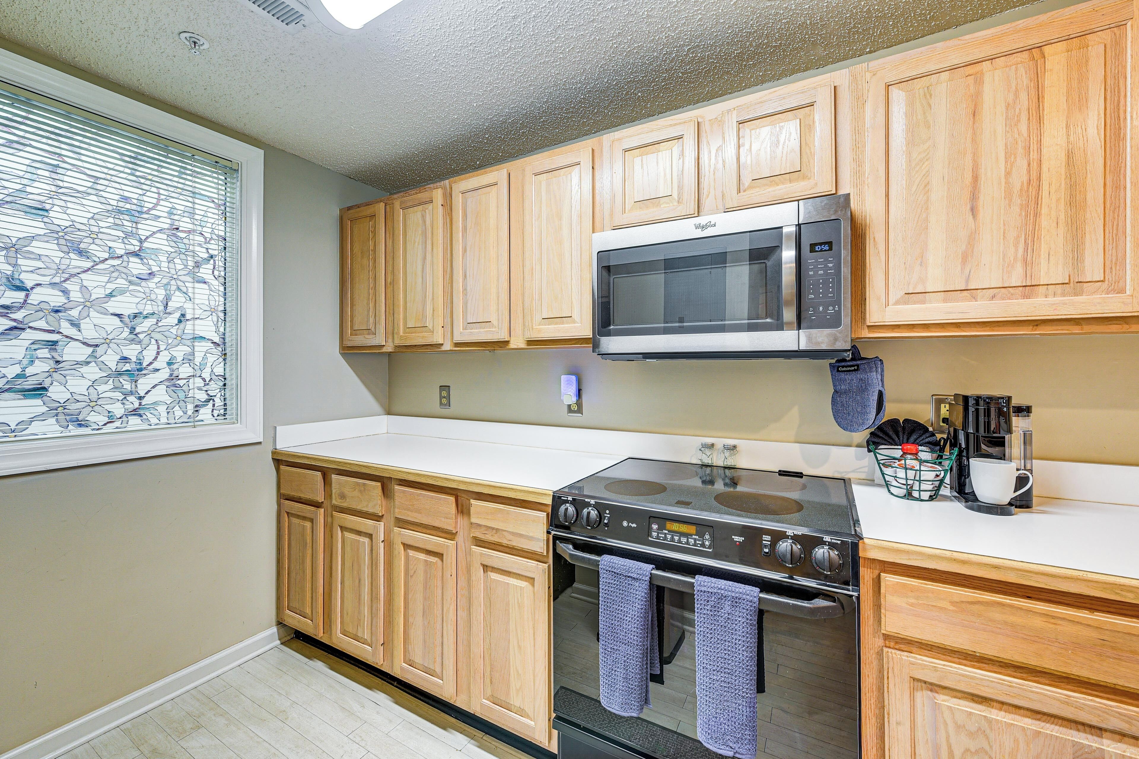 A kitchen with wooden cabinets, a microwave, an oven, and a window with decorative blinds.