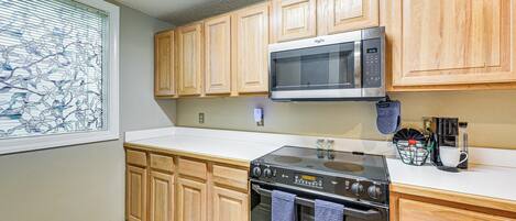 A kitchen with wooden cabinets, a microwave, an oven, and a window with decorative blinds.