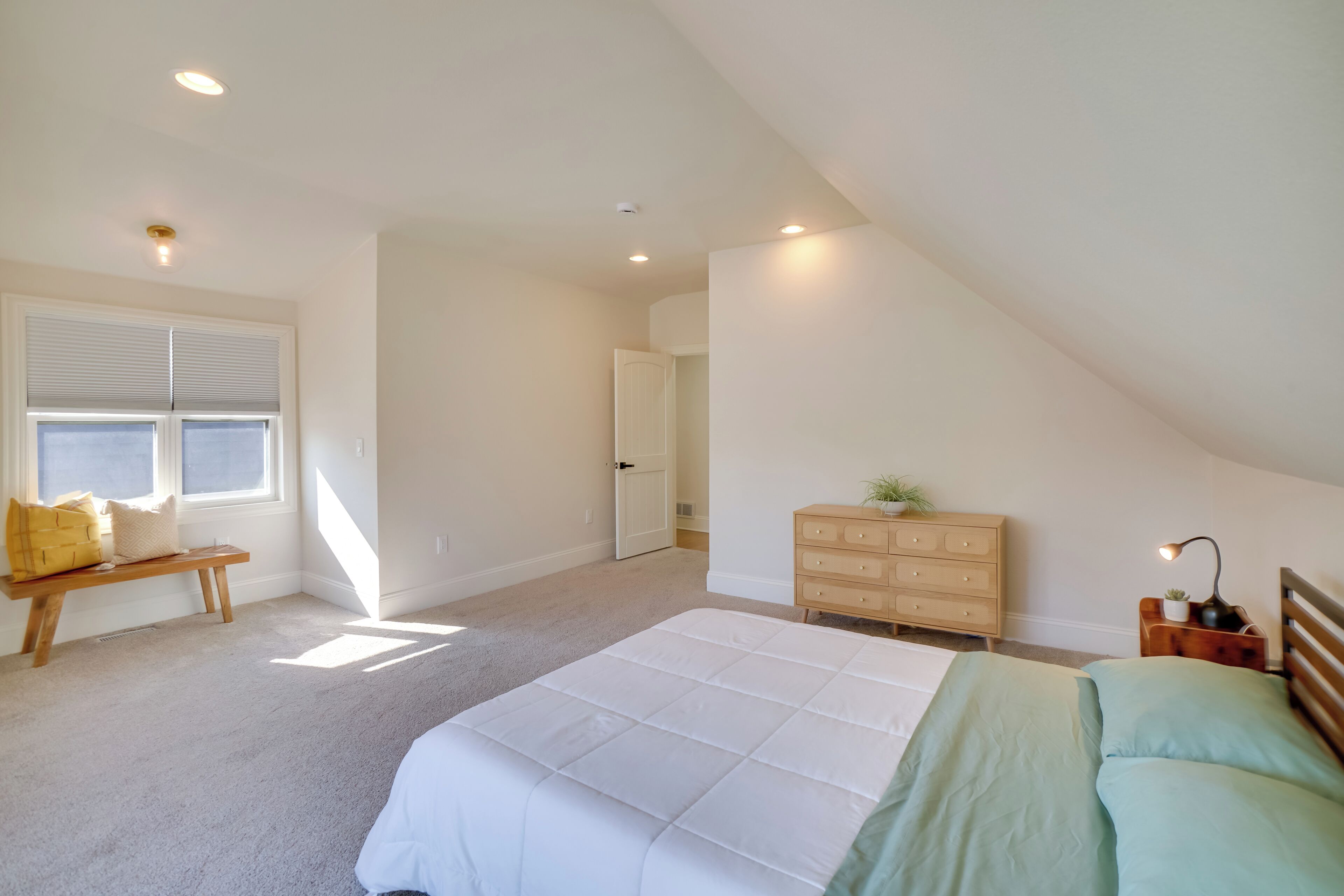 A bedroom with a large bed, a bench, a dresser, and a nightstand.