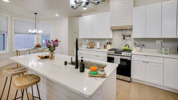 A modern kitchen with white cabinetry, a large island with stools, a chandelier, and a stove. - Heart of Bay View Neighborhood! Modern Retreat (Milwaukee)