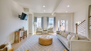 A spacious living room with a large sofa, a round ottoman, and a television mounted on the wall. There are two chairs and a small table with decorative items. - Heart of Bay View Neighborhood! Modern Retreat (Milwaukee)