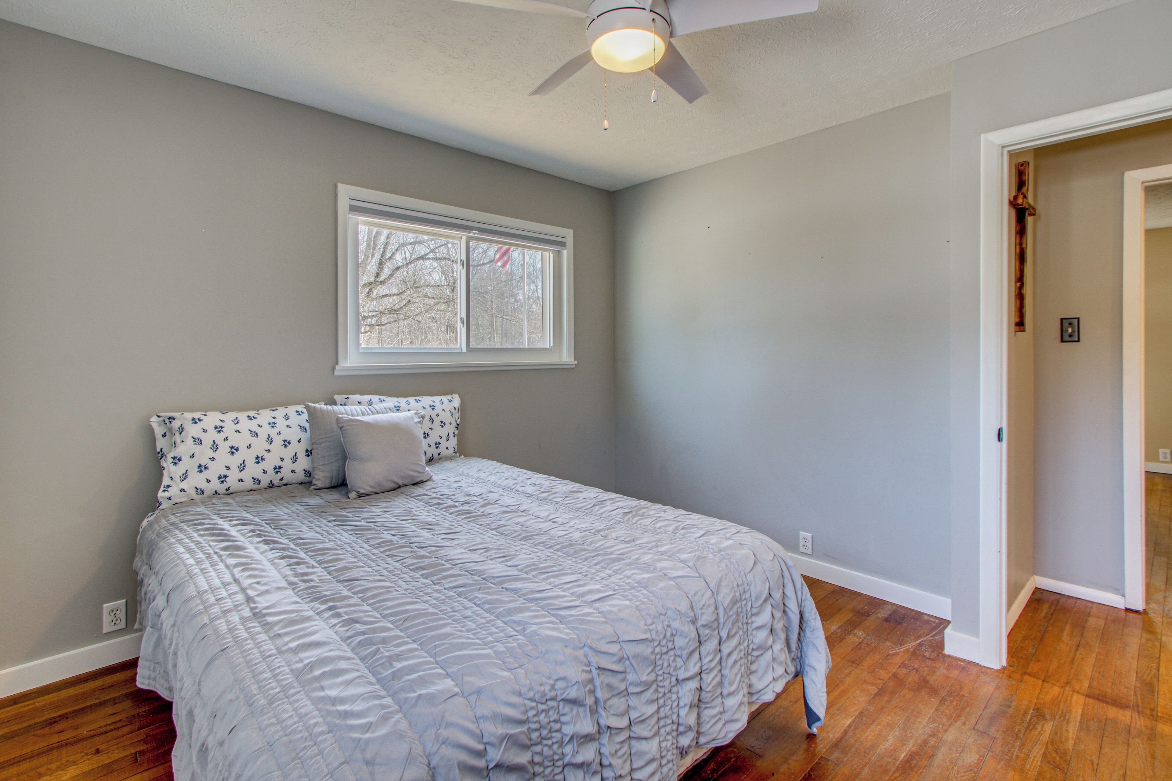 A bedroom with a bed, a ceiling fan, a window, and hardwood flooring.