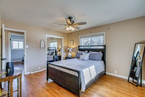 Une chambre avec un plancher en bois, un lit doté d’une tête de lit sombre, un ventilateur de plafond et une fenêtre.