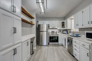 Une cuisine moderne avec des meubles blancs, des appareils en acier inoxydable et une étagère en bois.
