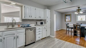 A modern kitchen with white cabinets, a dishwasher, and a microwave. There is a dining area with a table and chairs. - Peaceful Retreat w/ Private Hot Tub in New Albany (New Albany)