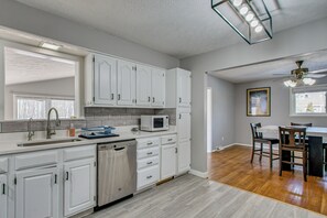 A modern kitchen with white cabinets, a dishwasher, and a microwave. There is a dining area with a table and chairs. - Peaceful Retreat w/ Private Hot Tub in New Albany (New Albany)