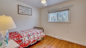 A bedroom with a wooden floor, a bed with a floral quilt, a ceiling fan, a window with blinds, and a motivational quote on the wall. - Peaceful Retreat w/ Private Hot Tub in New Albany (New Albany)