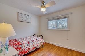 A bedroom with a wooden floor, a bed with a floral quilt, a ceiling fan, a window with blinds, and a motivational quote on the wall. - Peaceful Retreat w/ Private Hot Tub in New Albany (New Albany)