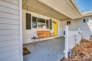 A porch with a wooden bench, a small table, and a yellow door.