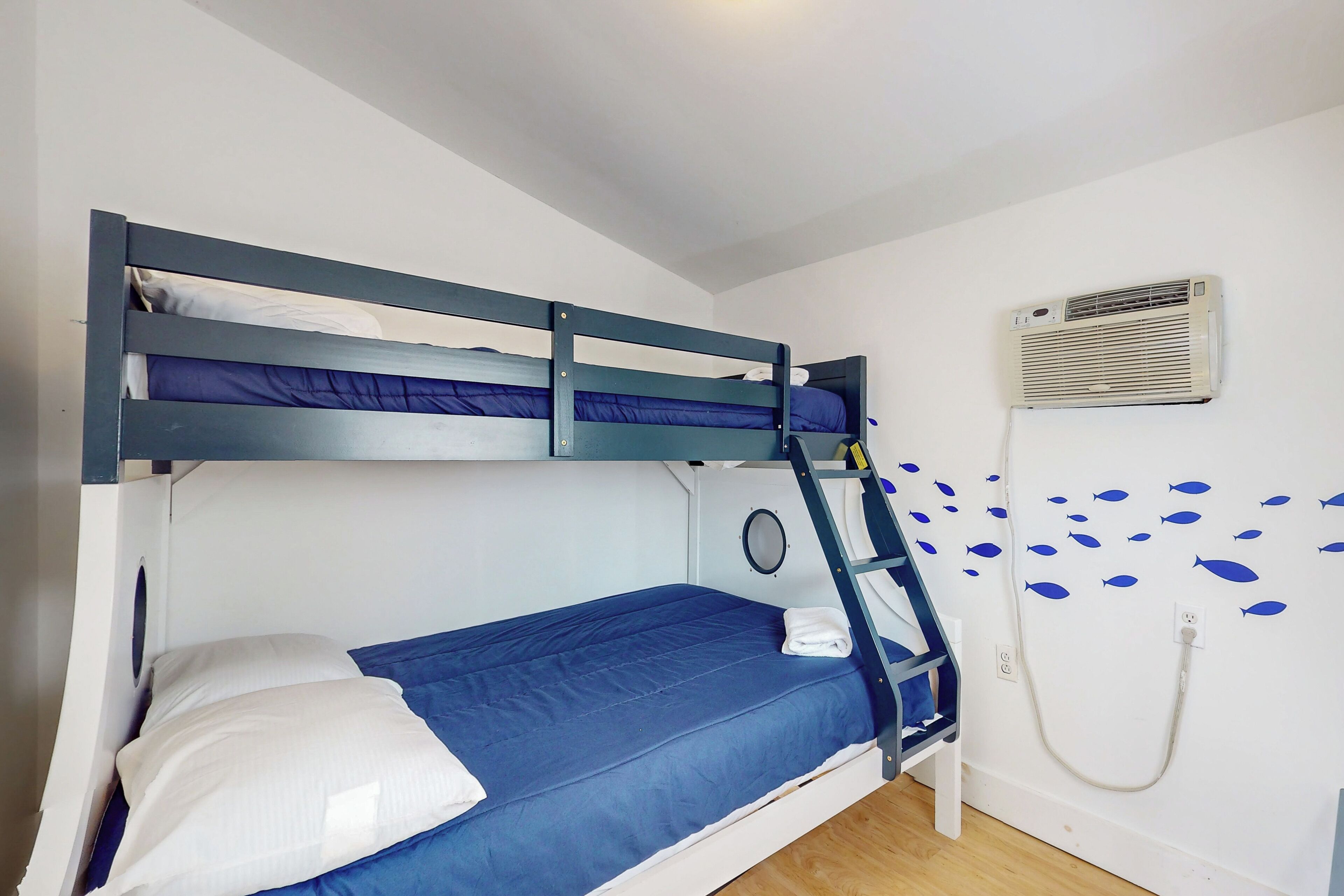 Una cama litera con escalera, un aire acondicionado de pared y una pared decorada con calcomanías de peces.
