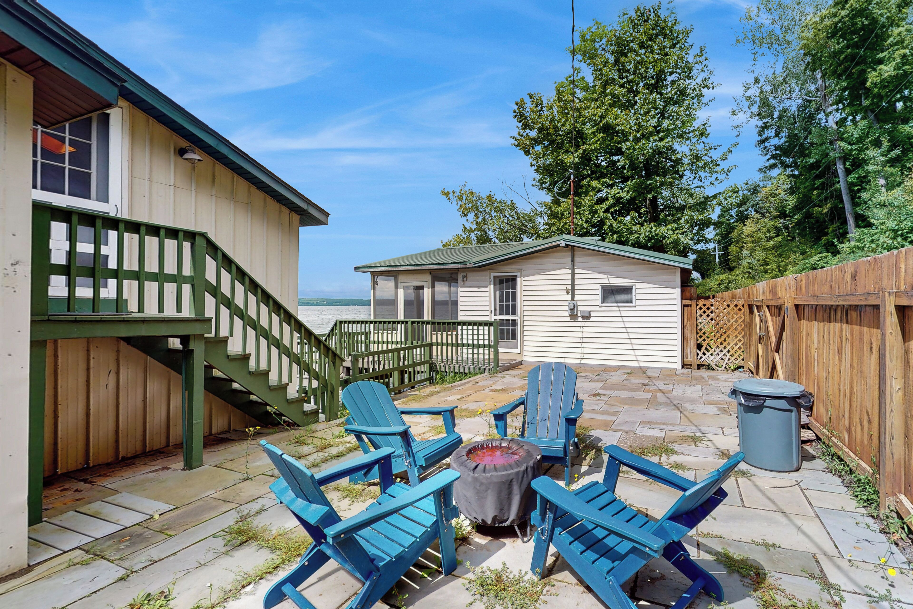 A patio with blue Adirondack chairs, a small fire pit, and a wooden fence.