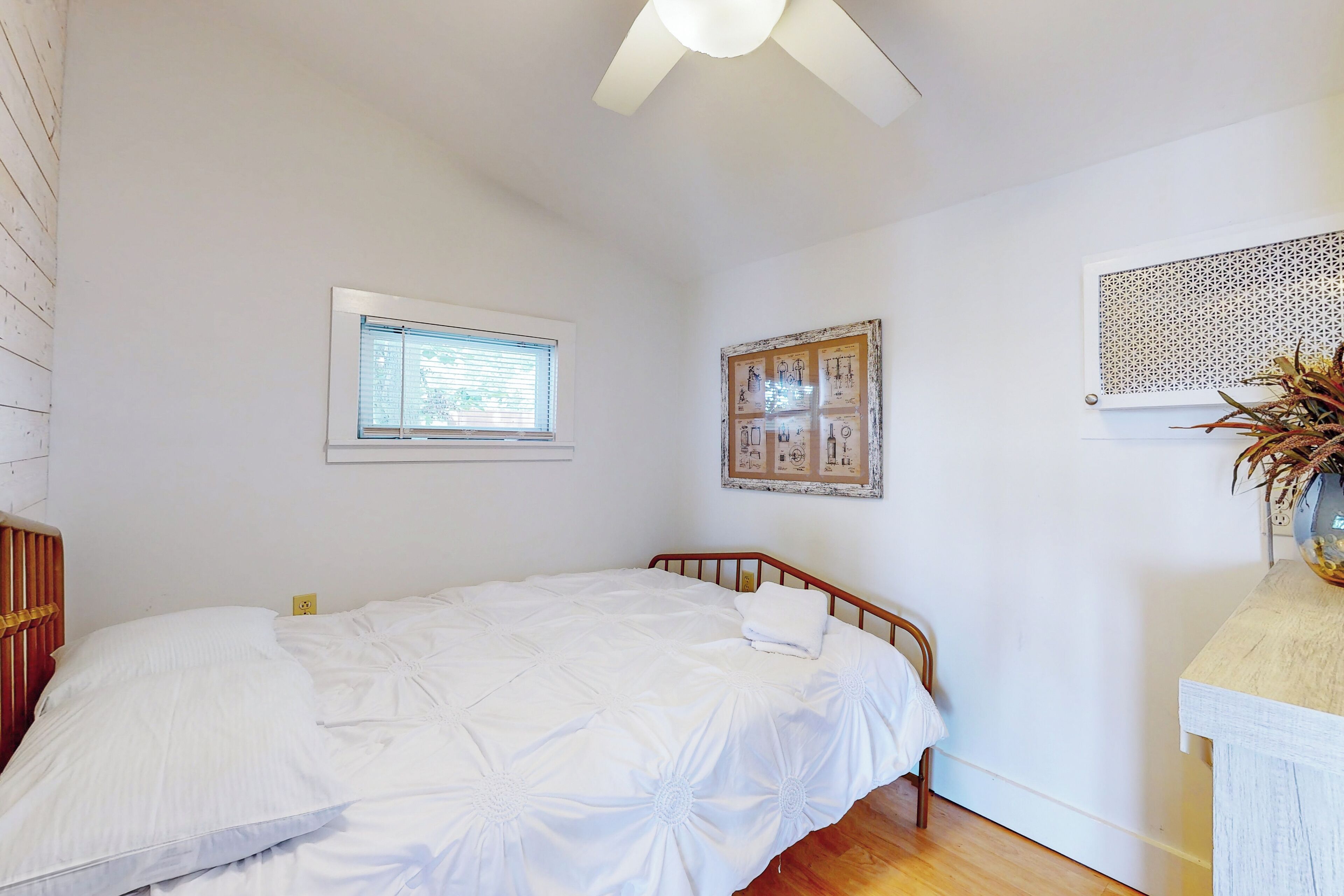 A bedroom with a wooden bed, a window, a ceiling fan, and a wall-mounted decorative panel.